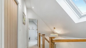 Un pasillo estrecho con suelo de madera, pared blanca y tragaluz.