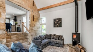 Una sala de estar acogedora con pared de piedra, un sofá seccional grande, una chimenea y un televisor montado en la pared.