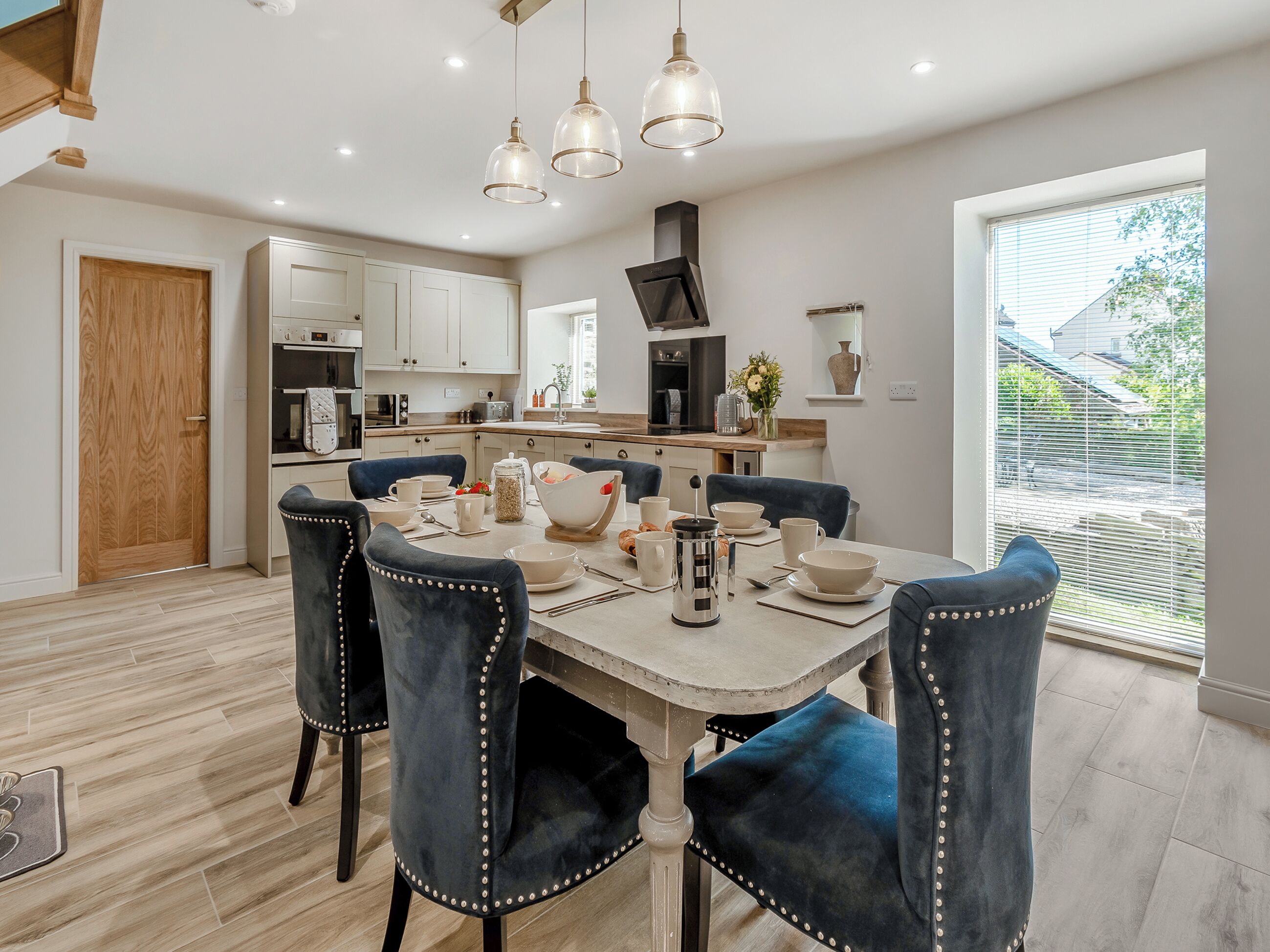 A modern dining area with a wooden door, white cabinets, and a kitchen in the background.
