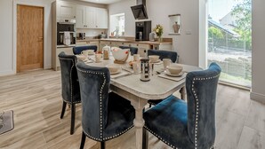 Un comedor moderno con puerta de madera, armarios blancos y una cocina al fondo.