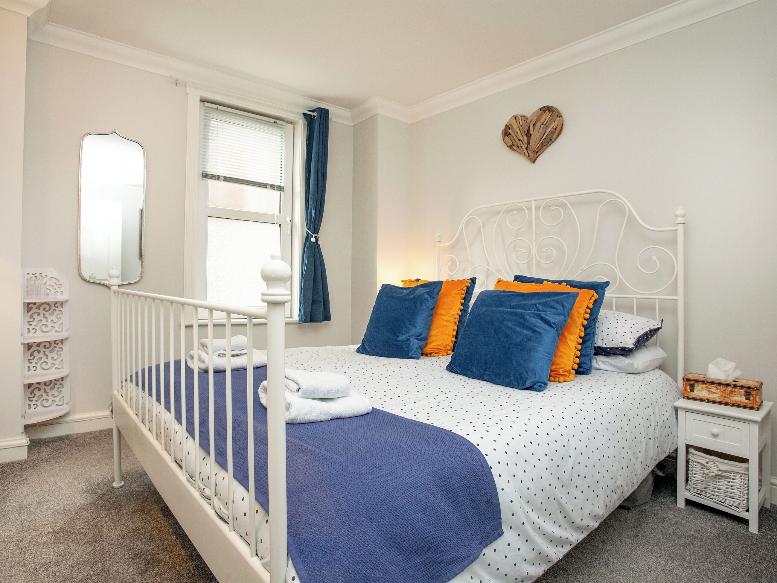 Una camera da letto con un letto con struttura in metallo bianco, una coperta a pois blu e bianchi e cuscini coordinati.
