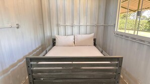 Una cama con estructura de madera y ropa de cama blanca en una habitación con suelo de madera y pared de metal corrugado.