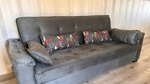 Un canapé en cuir gris, agrémenté de deux coussins à motifs, placé contre un parquet et un mur blanc.