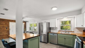 Una cocina moderna con armarios verdes, electrodomésticos de acero inoxidable y una isla de madera.