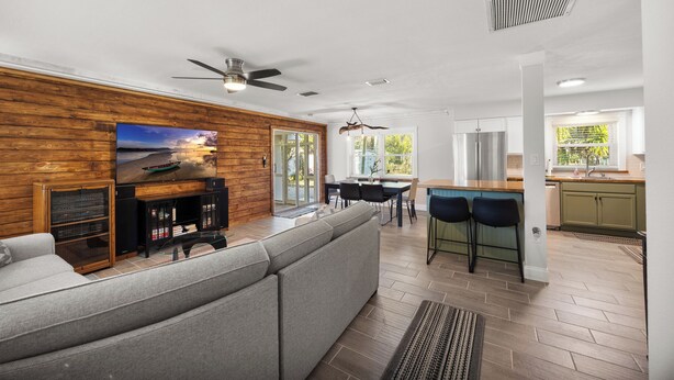 Una sala de estar moderna con un sofá gris, paneles de madera en la pared, un ventilador de techo y un televisor.