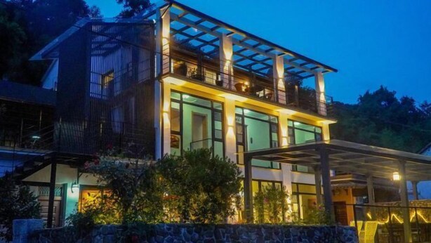 A modern two-story building with a glass facade, a balcony on the upper floor, and a stone wall in the foreground. - Mojia Inn (Deqing)