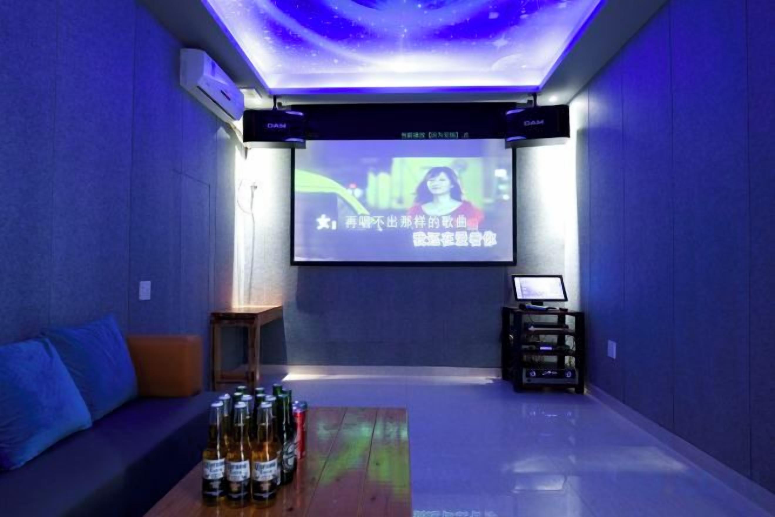 A room with a projection screen, a sofa, a coffee table with bottles, and a small table with electronic devices.