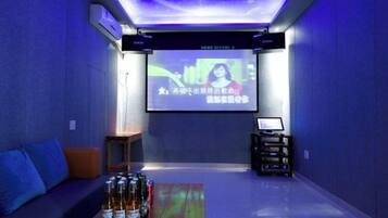 A room with a projection screen, a sofa, a coffee table with bottles, and a small table with electronic devices.
