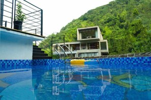 Une piscine dotée d’une plateforme de plongeon et d’un escalier menant à un bâtiment avec un balcon.