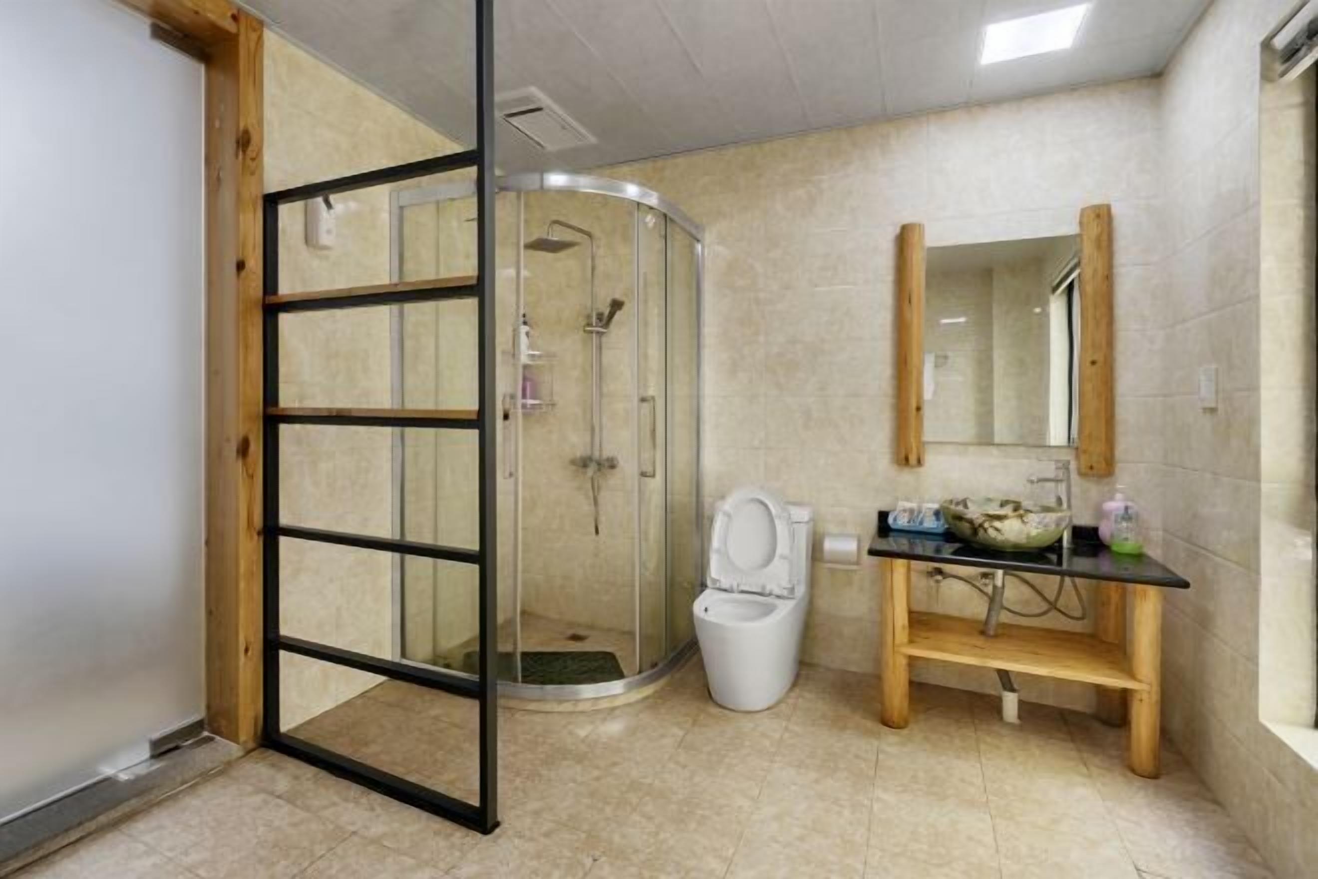 A bathroom with a glass shower enclosure, a toilet, a sink with a mirror, and wooden shelves.