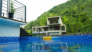A swimming pool with a blue tiled edge, a metal ladder, and a modern building with large windows in the background. - Mojia Inn (Deqing)