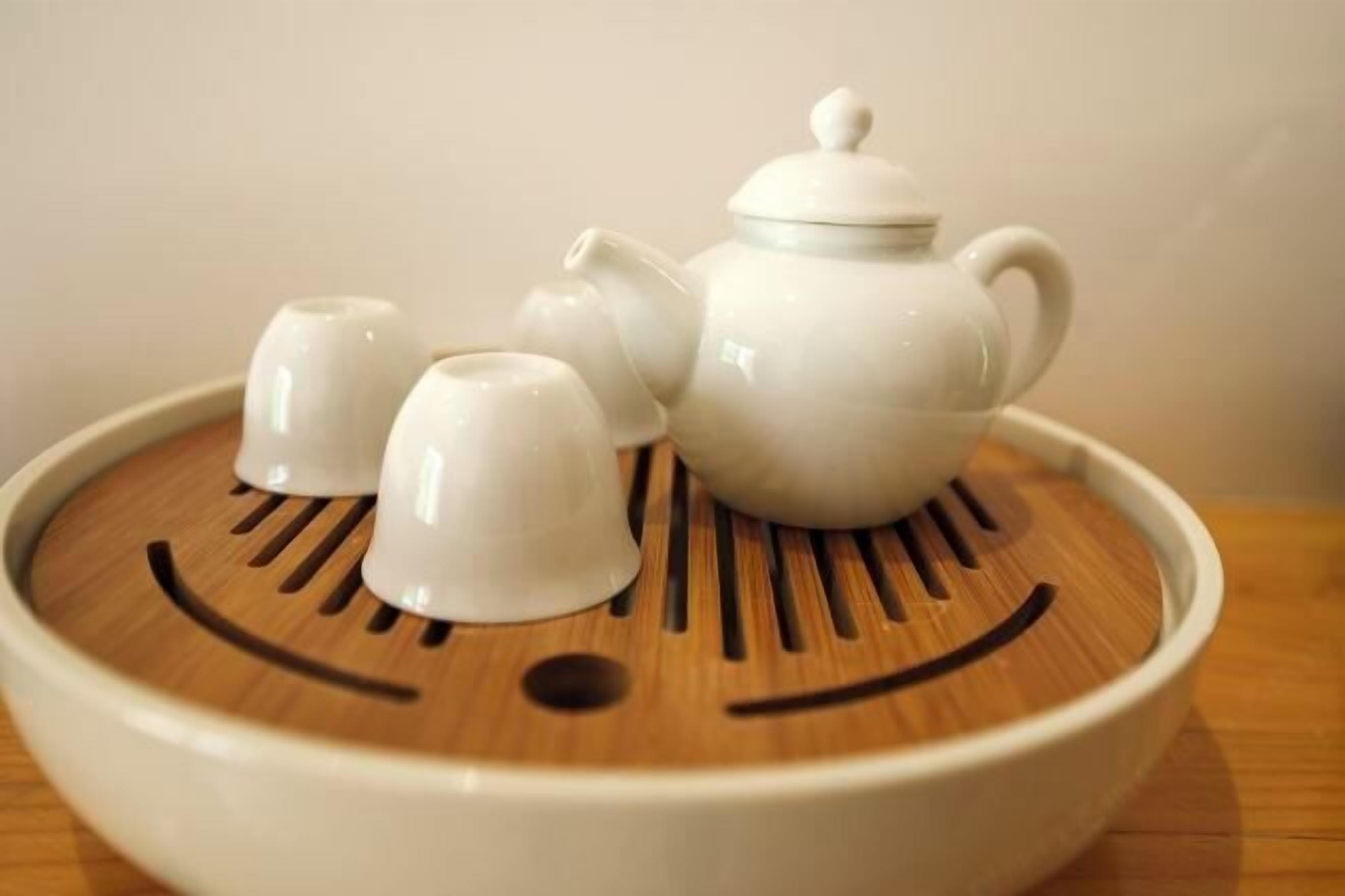 A white teapot set on a wooden tray with a smiley face design.