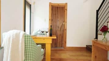A small, cozy room with a wooden door, a dining table with a bottle and glasses, a chair, and a staircase with a vase of flowers.
