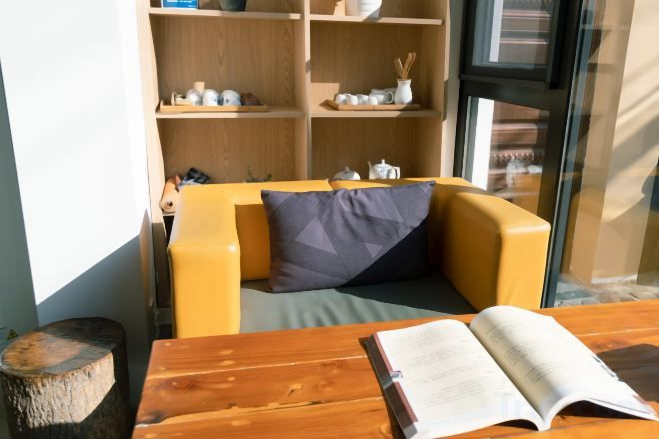 A room with a wooden table, a sofa with cushions, and a bookshelf with decorative items.