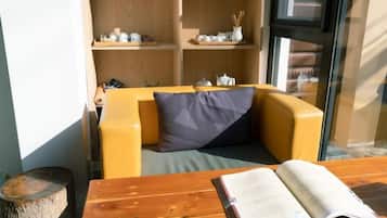 A room with a wooden table, a sofa with cushions, and a bookshelf with decorative items.