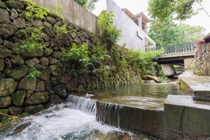 Un muro de piedra con una cascada pequeña, un puente y un edificio al fondo.