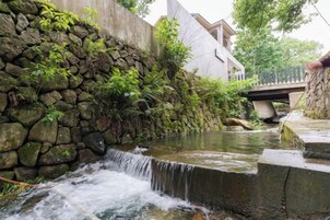 A stone wall with a small waterfall, a bridge, and a building in the background.