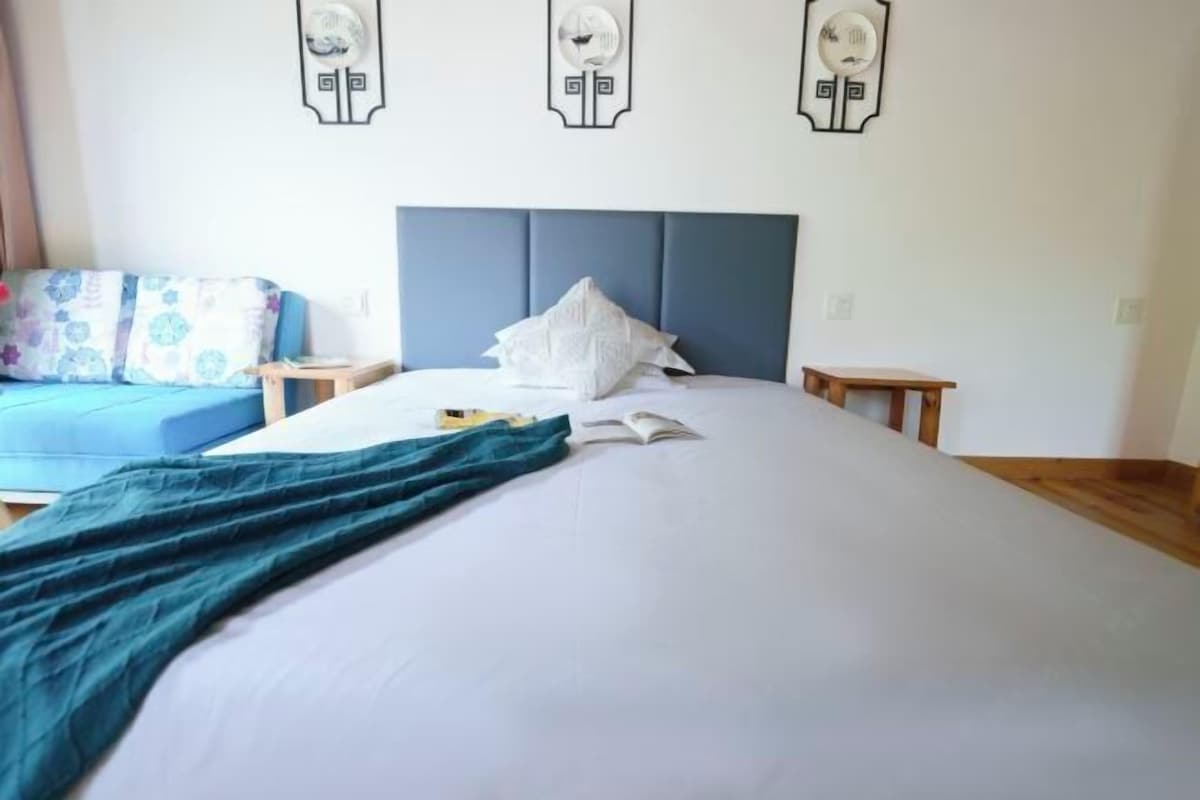 A neatly made bed with a blue headboard, a bedside table, and a wall clock.