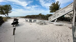 Une terrasse au bord de la plage, dotée de sièges extérieurs et d’un escalier menant à un bâtiment.