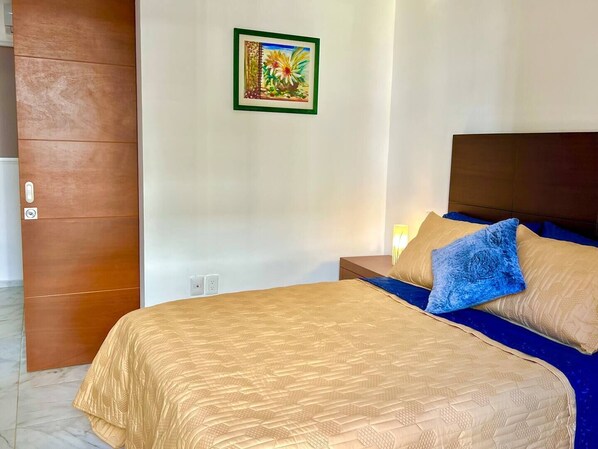 A hotel room with a bed, a nightstand, a wall-mounted painting, and a wooden door.