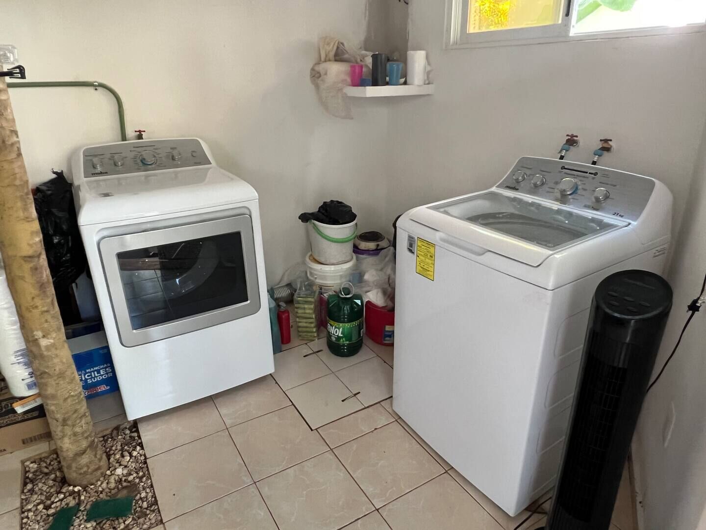 Een wasruimte met twee witte wasmachines, een klein plankje met toiletartikelen en een raam erboven.