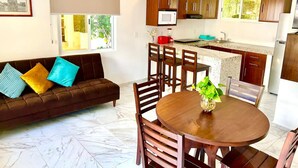 Una cocina moderna con armarios de madera, un comedor con una mesa redonda y un sofá con cojines de colores.