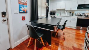 Una cocina moderna con gabinetes blancos, encimera negra y comedor con mesa y sillas negras.
