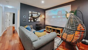 Una sala de estar moderna con un sofá gris, una pantalla de proyector mostrando una caricatura y una lámpara metálica decorativa.