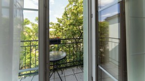 A balcony with a table and chairs, surrounded by a metal railing, overlooking a garden with trees and a clear sky. - Hotel Raffaello Prague (Prague)