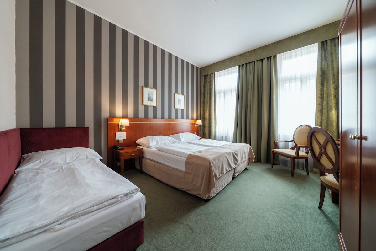 A hotel room with two beds, a wooden headboard, a desk with a lamp, a chair, and a wardrobe.