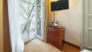 A room with a sliding glass door leading to a balcony, a flat-screen TV mounted on the wall, and a wooden cabinet with a coffee maker and a bottle. - Hotel Raffaello Prague (Prague)
