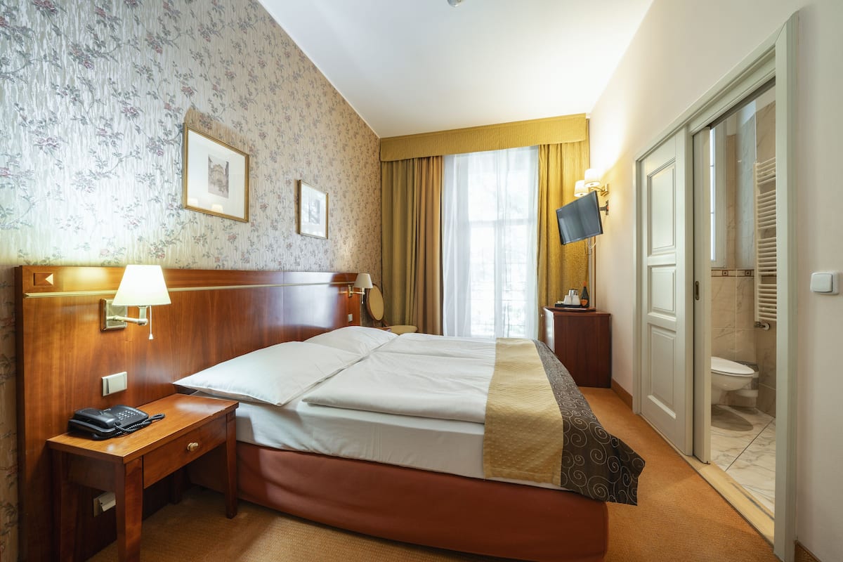 A hotel room with a bed, bedside table, lamp, and a television.