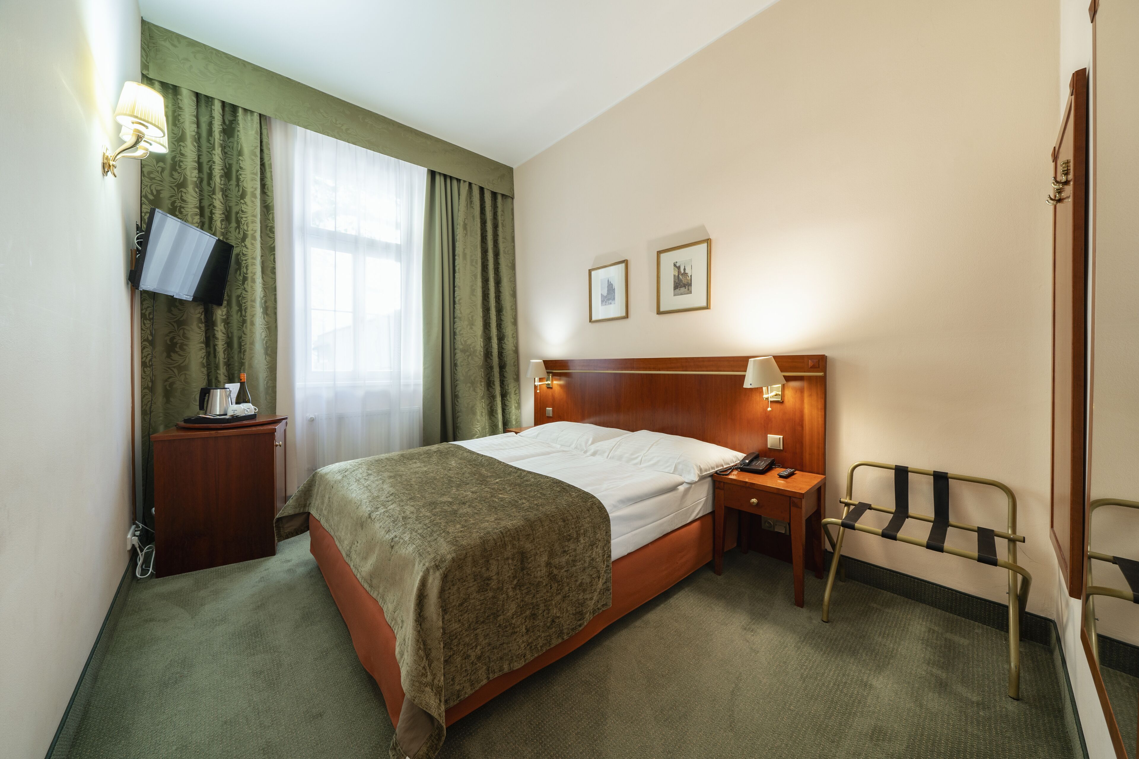 Una habitación de hotel con cama, mesita de noche, lámpara y televisor montado en la pared.