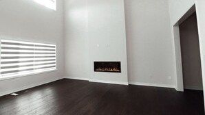 Ein Zimmer mit dunklem Holzboden, weißen Wänden, einem Kamin und einem Fenster mit Jalousien.