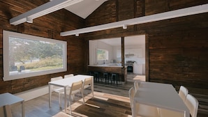 Un interior moderno con paredes de madera, un ventanal grande, un comedor y una cocina visible a través de un vano abierto.