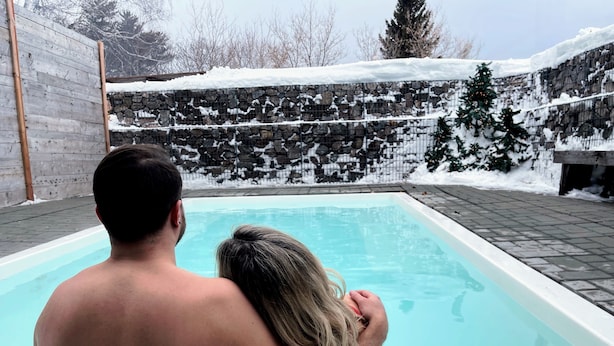 Una piscina con un muro de piedra y una valla de madera al fondo.