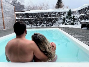Una piscina con un muro de piedra y una valla de madera al fondo.