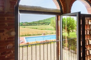 A view through an open door with a metal railing, leading to a swimming pool and a grassy field.