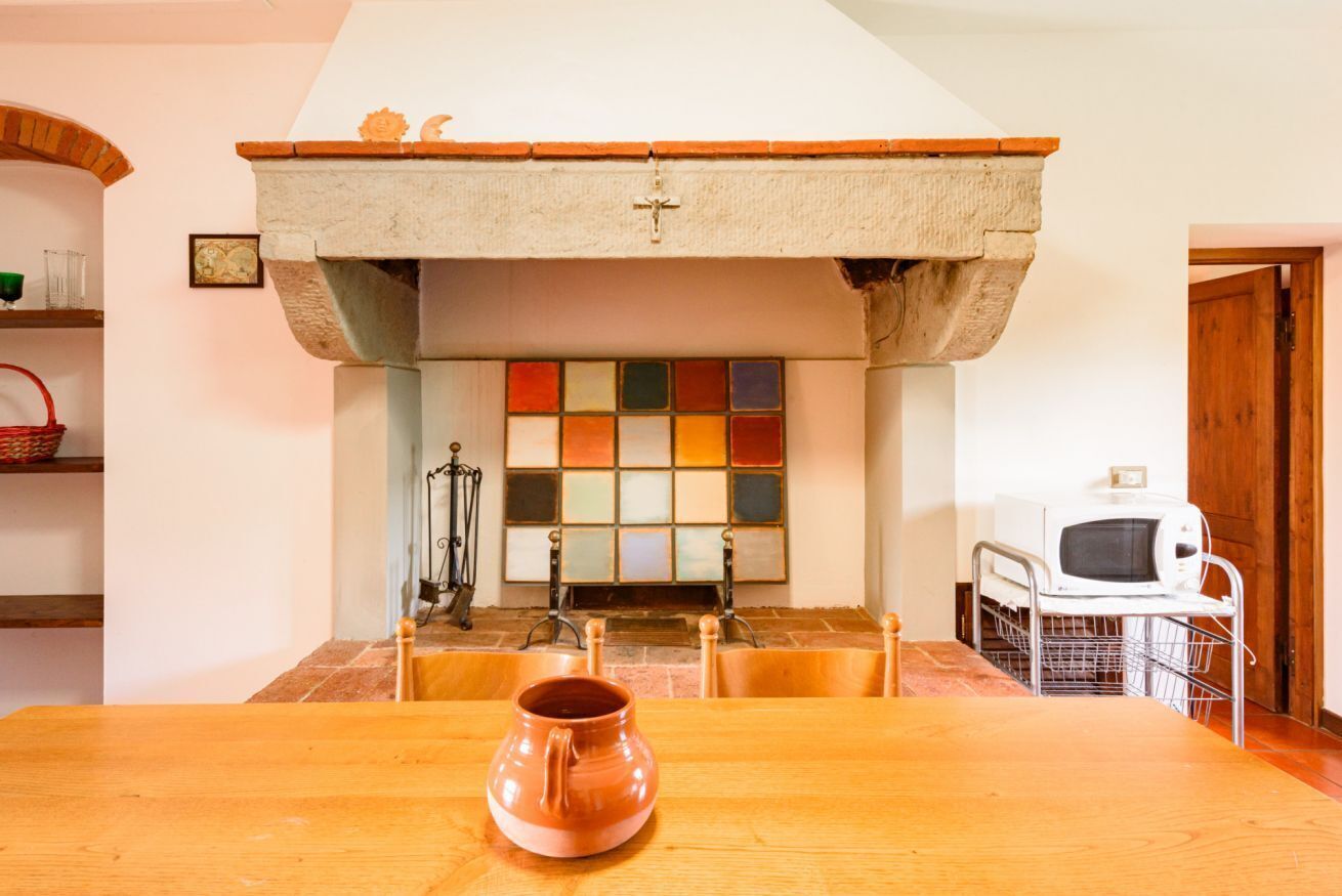 A dining area with a wooden table, a ceramic pitcher, a tiled fireplace, and a white microwave.
