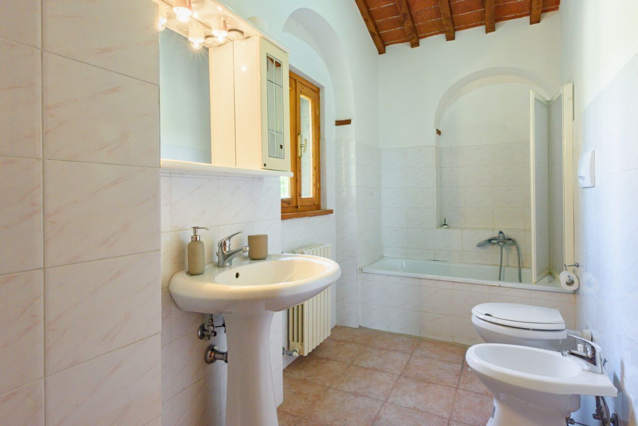 A bathroom with a sink, two toilets, a bathtub, and a window.
