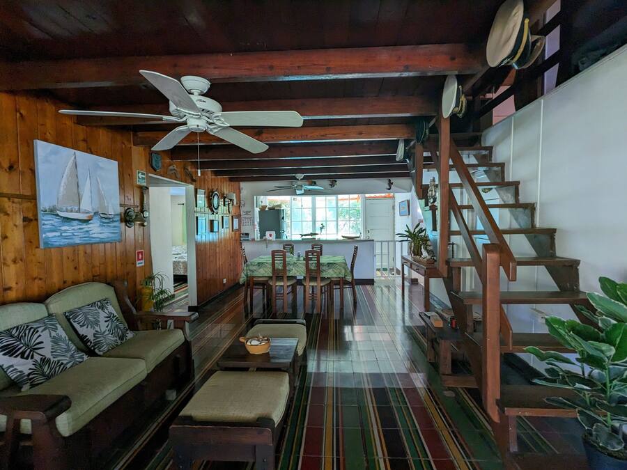 Una sala de estar acogedora con techo de madera, una zona de comedor con sillas y una mesa, y una escalera que sube.