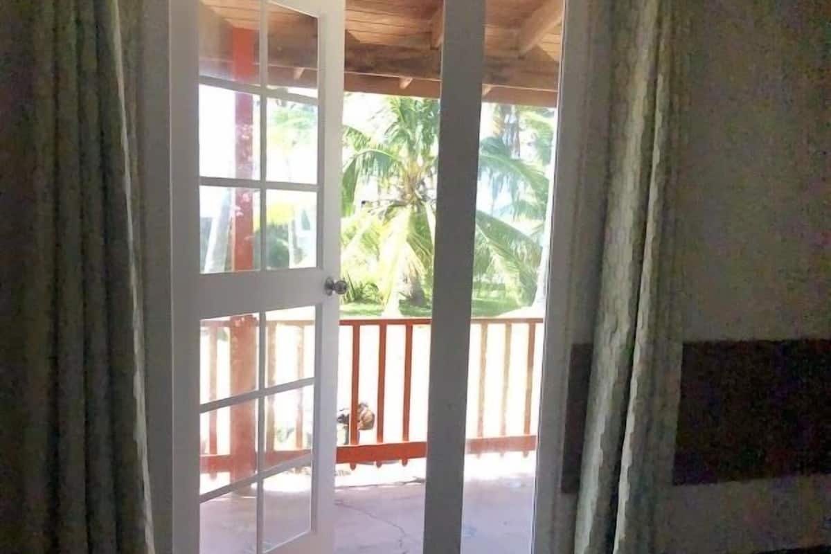 A room with a bed, a door leading to a balcony, and a view of palm trees.