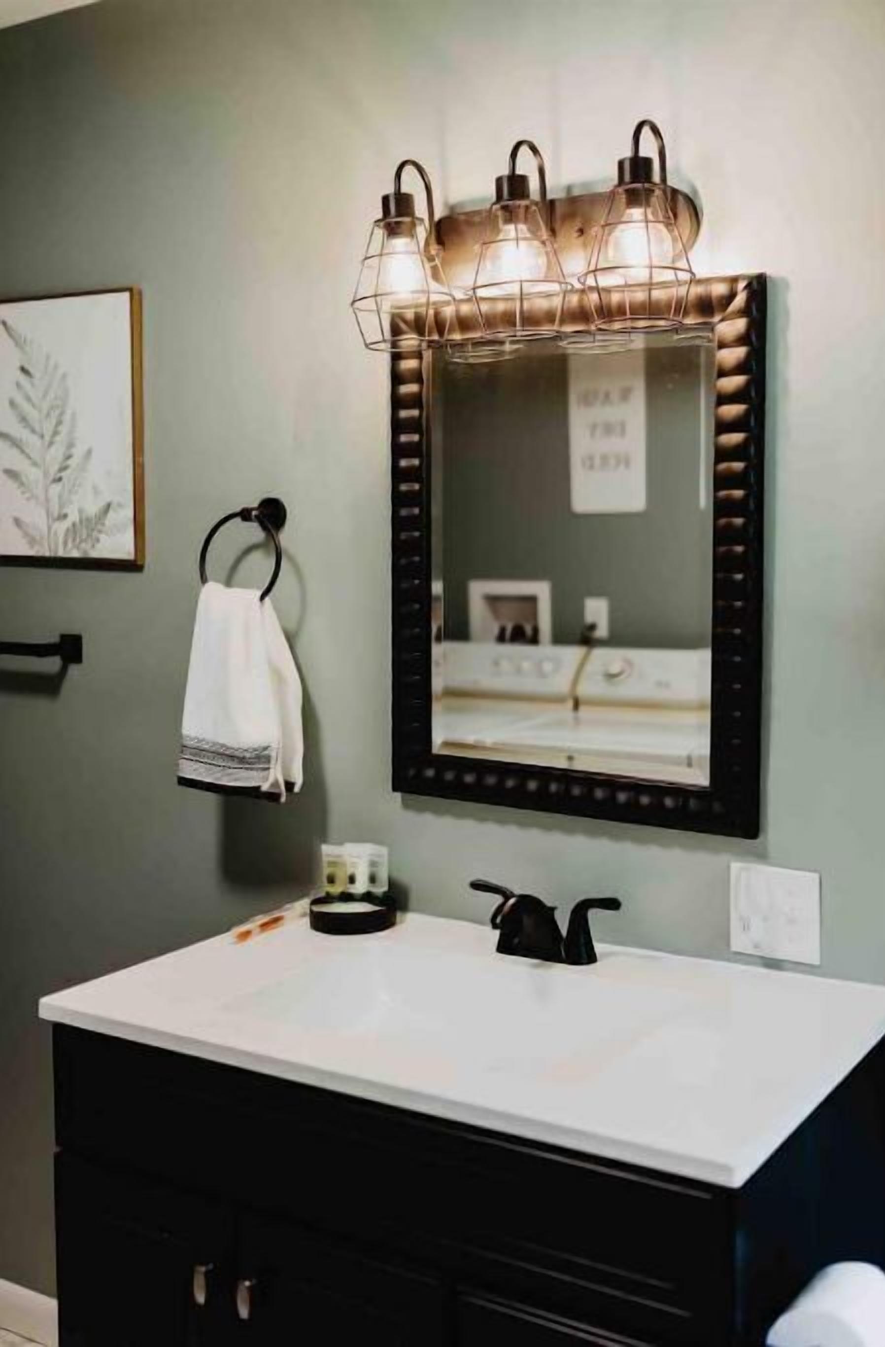 Une salle de bain avec un lavabo blanc, un meuble noir, un porte-serviettes avec une serviette blanche et un miroir avec un cadre noir.