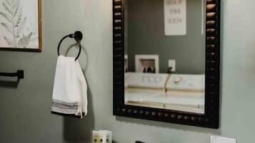 Une salle de bain avec un lavabo blanc, un meuble noir, un porte-serviettes avec une serviette blanche et un miroir avec un cadre noir.