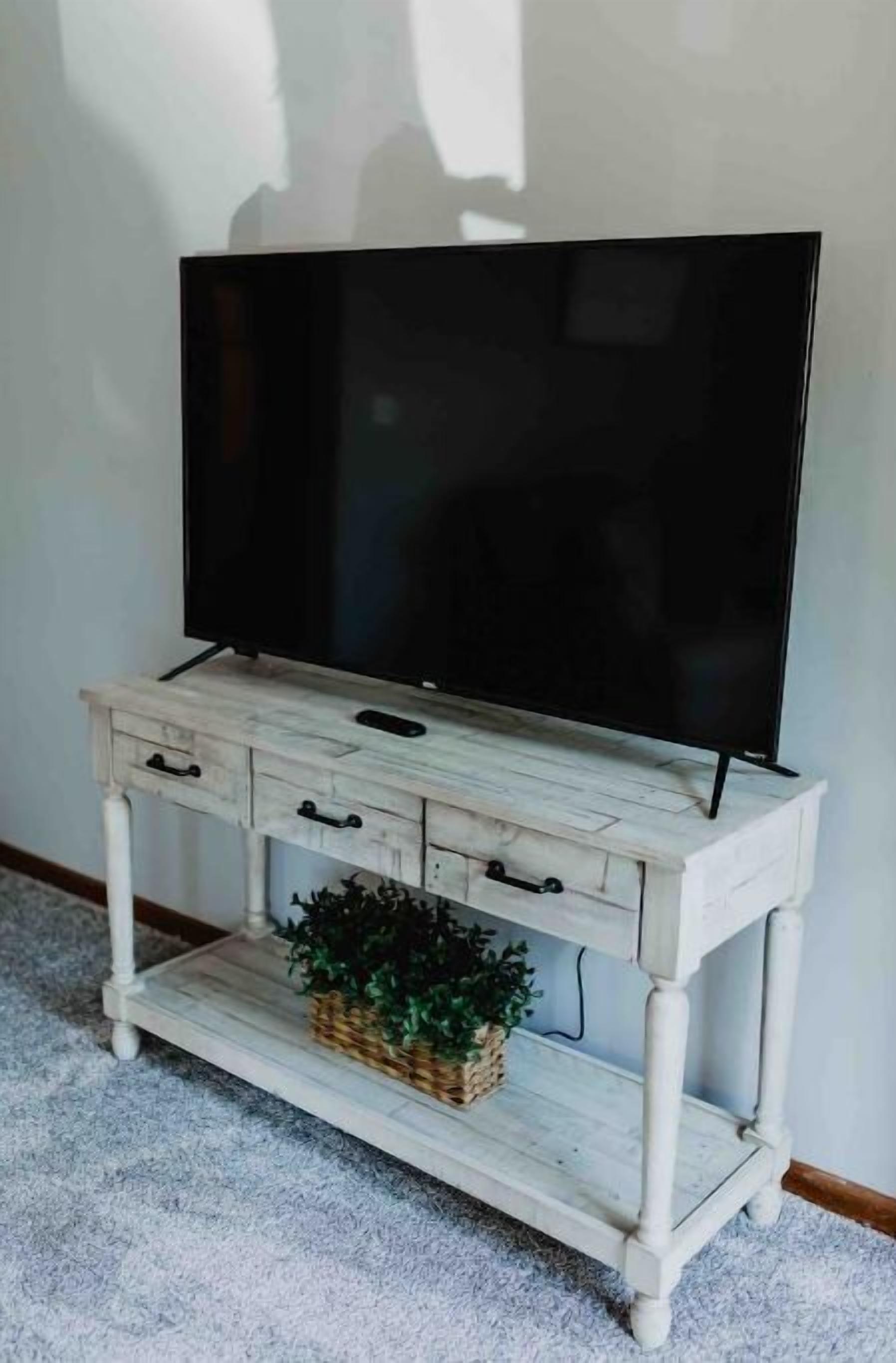 A white wooden TV stand with a flat-screen TV, drawers, and a small plant.