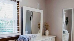 A bedroom with a white dresser, a large mirror, and a window with blinds. - Rancher in Mont Alto (Mont Alto)