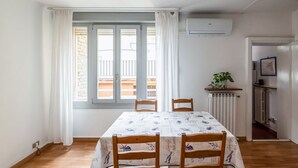 Un espace repas comprenant une table, des chaises, une plante en pot et donnant sur un balcon.