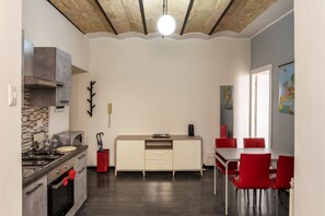 Une cuisine compacte équipée d’une cuisinière, d’un four et d’un four à micro-ondes. On y trouve un coin repas avec une table et des chaises rouges. La pièce est dotée d’un sol carrelé et d’une carte accrochée au mur.