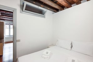 Un dormitorio con cama, ropa de cama blanca, una ventana y una viga de madera en el techo.