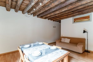 Un comedor con mesa de madera dispuesta para cuatro, un sofá color beige y una lámpara.
